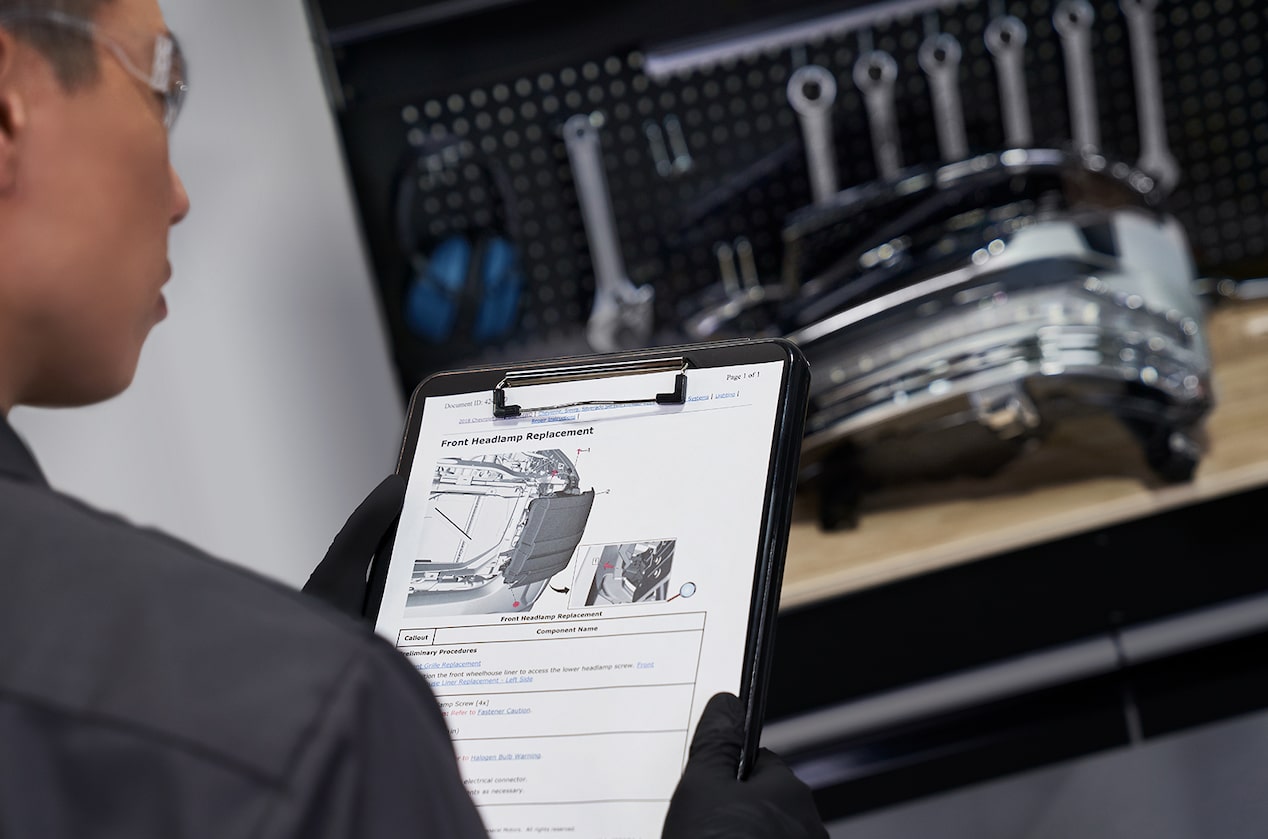 GM Technician Inspecting Clipboard With Car Parts Lying on Work Bench Nearby