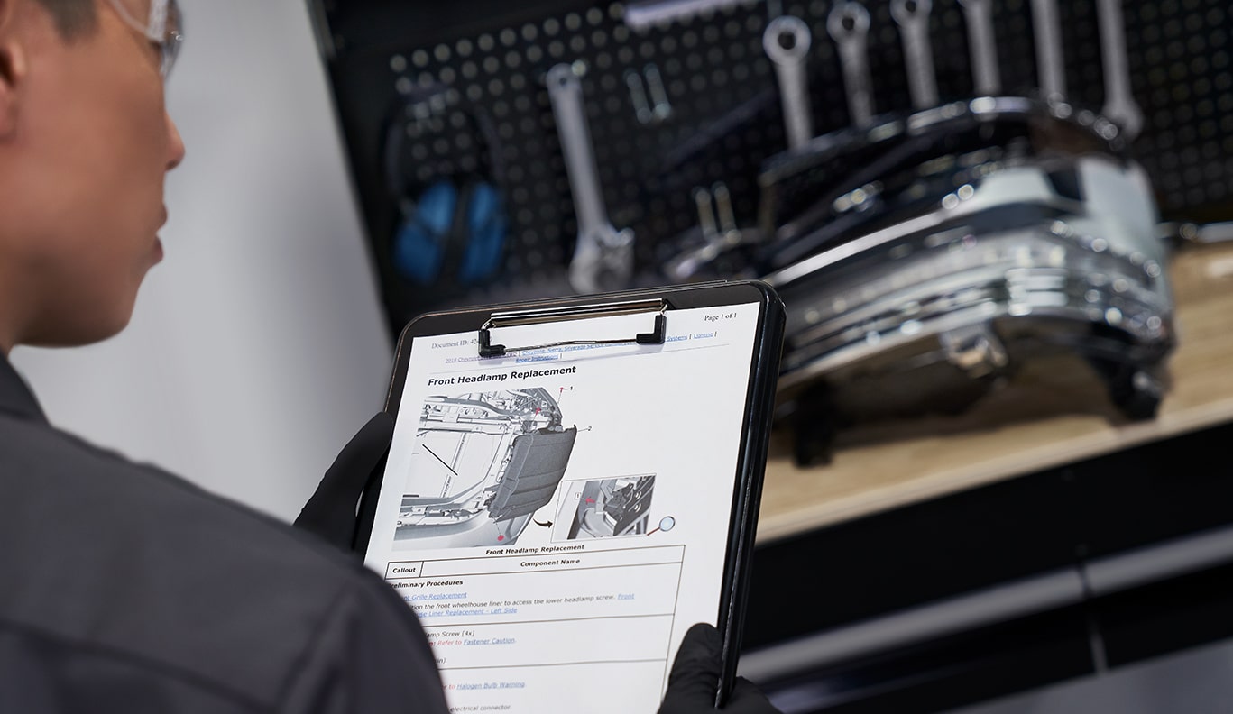 GM Technician Inspecting Clipboard With Car Parts Lying on Work Bench Nearby
