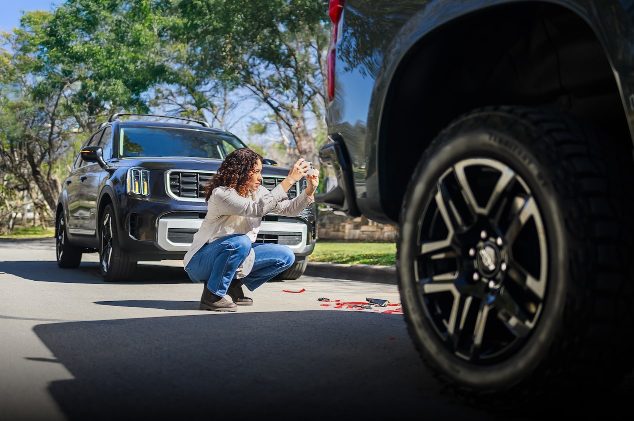 A Woman Crouching Down Taking a Picture of the Back of a Vehicle with Her Smartphone