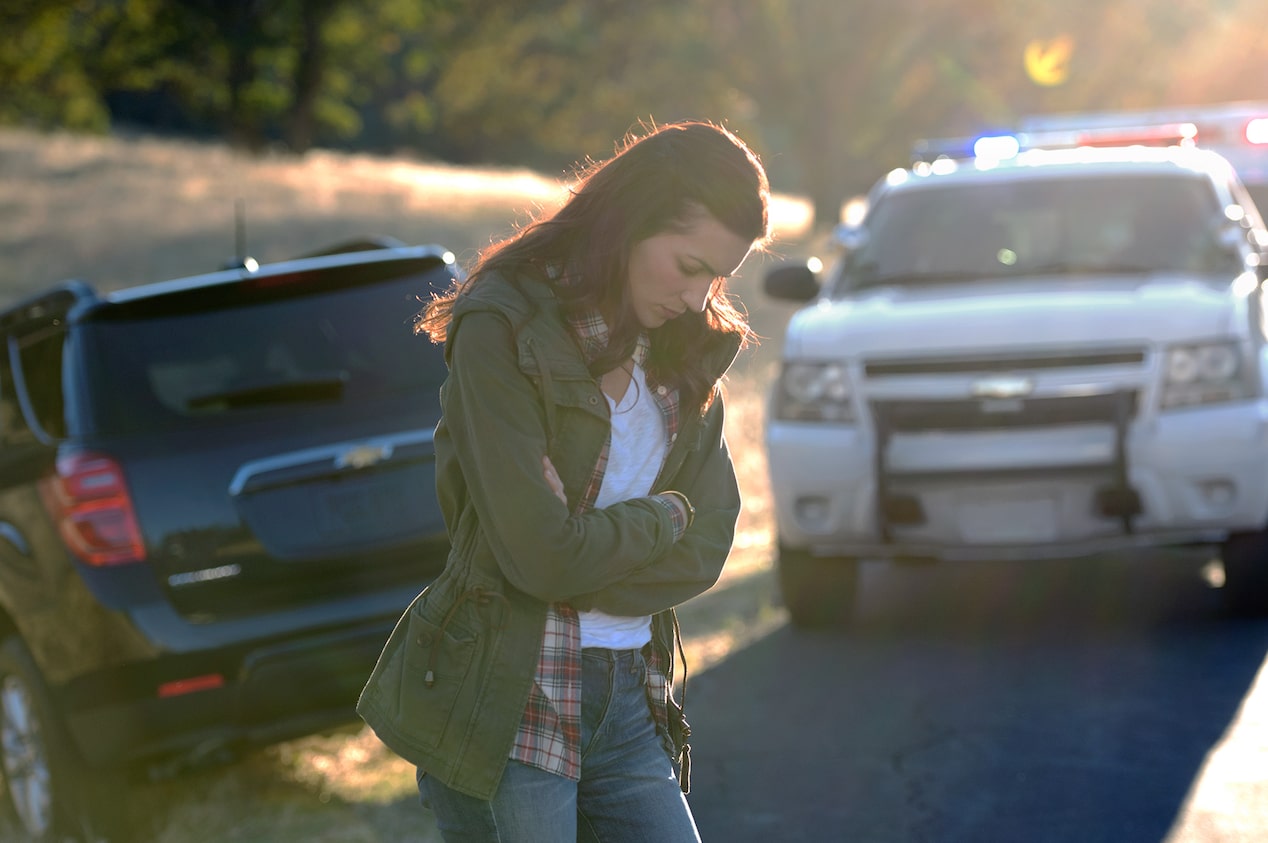 A Woman Standing Next to a Vehicle and A Police Vehicle