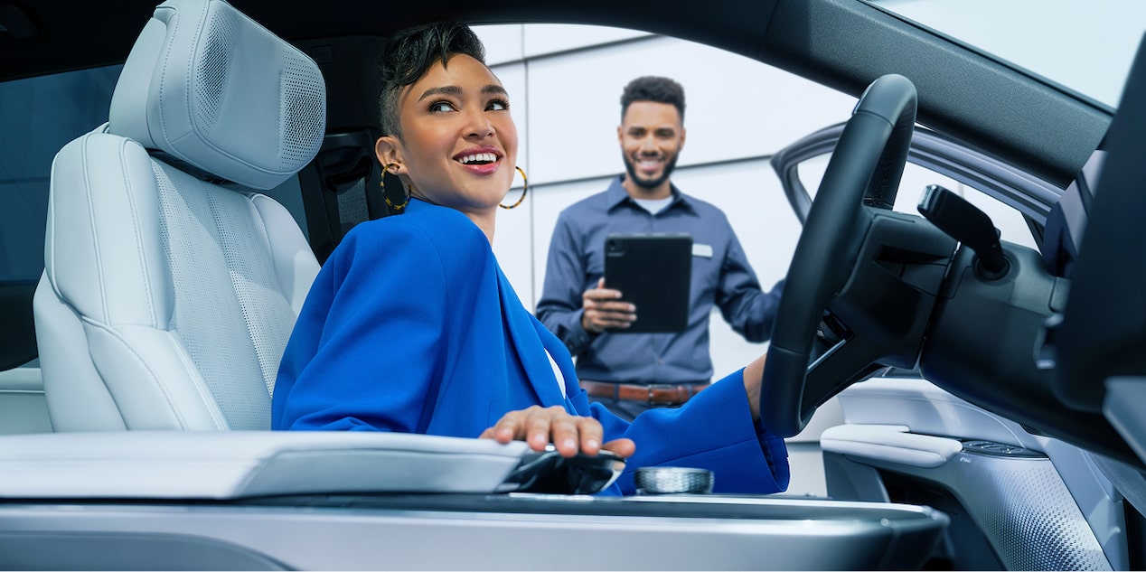 A Woman Sitting In The Drivers Seat Of A Vehicle While A Service Advisor Looks On.
