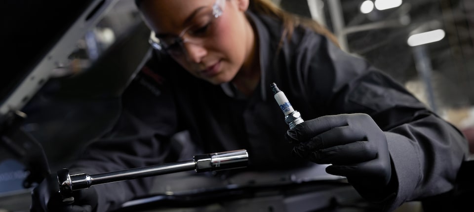 GM Technician Holding a Spark Plug and Working on a Vehicle