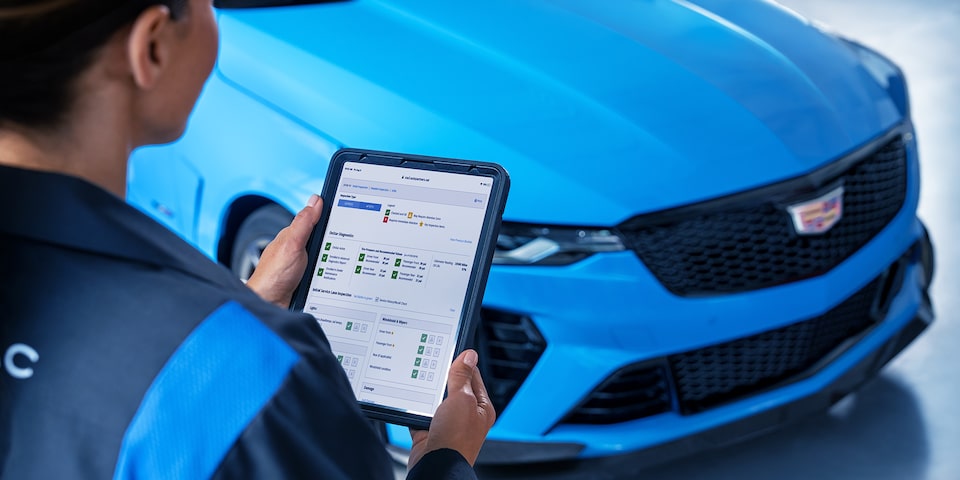 GM Technician Standing in Front of a Cadillac Vehicle Reviewing Vehicle Information on a Tablet