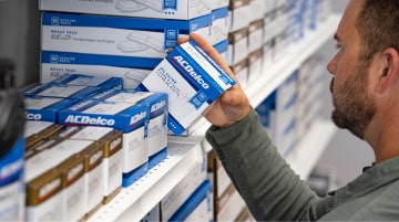 A man browses a retail shelf stocked with GM Genuine Parts and ACDelco automotive products, focusing on an ACDelco oil filter box held in his hand.
