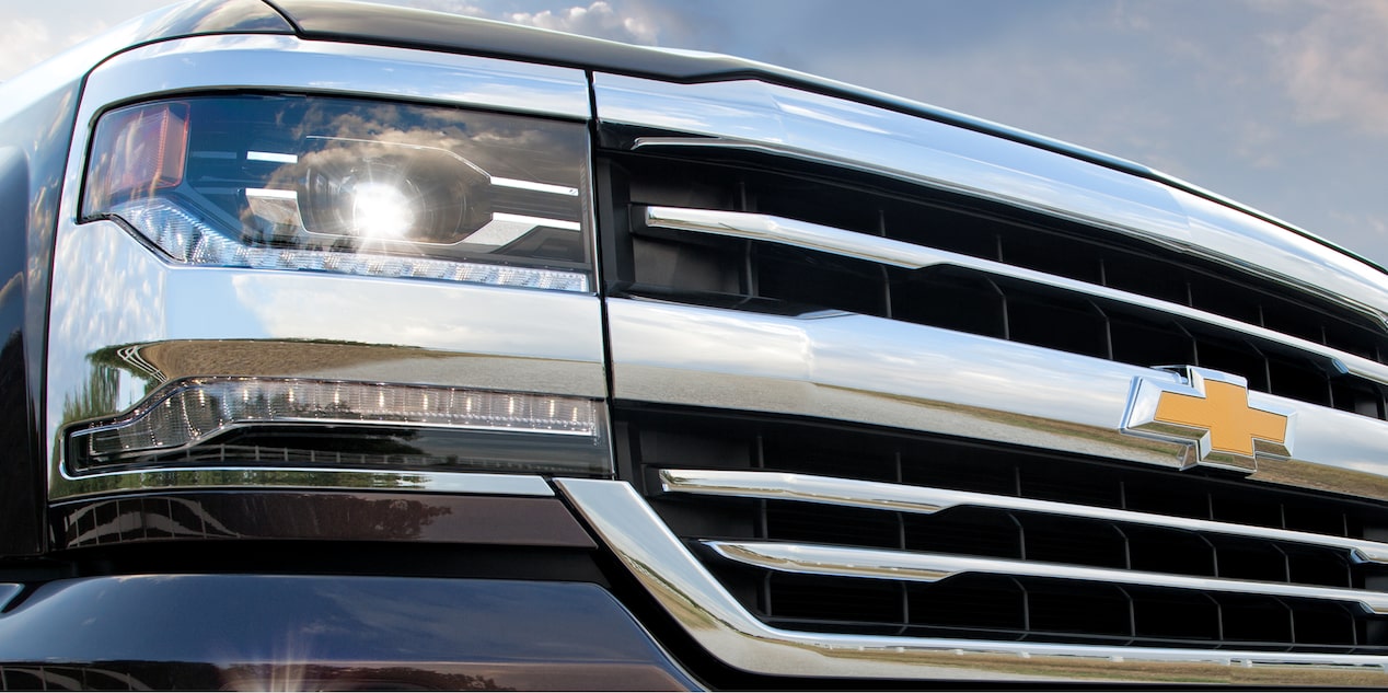 Angular Close-up View of a Chevrolet Vehicle Grille and Headlight Under a Blue Sky