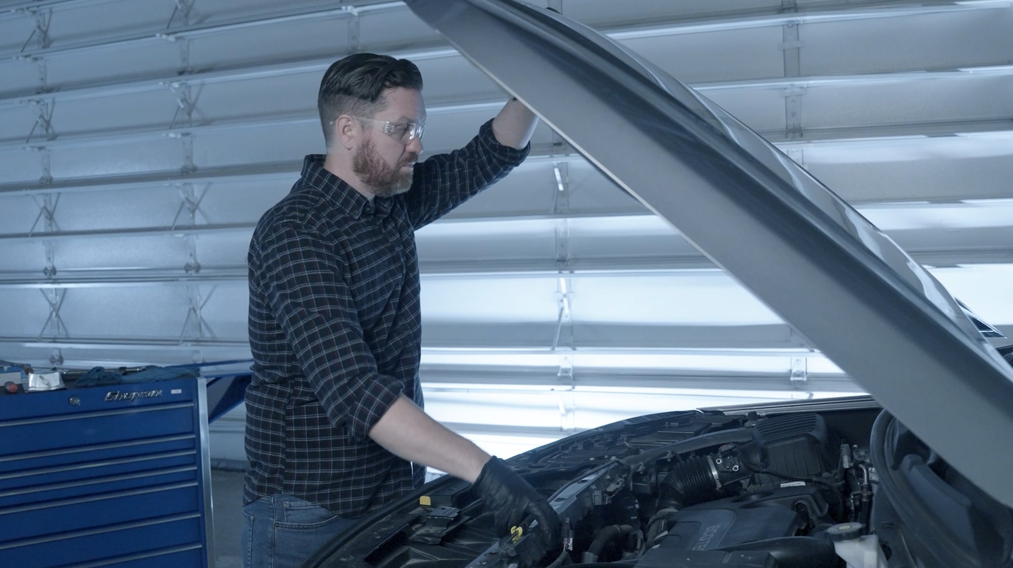A Mechanic is Observing the Engine of a Vehicle Holding its Hood Open