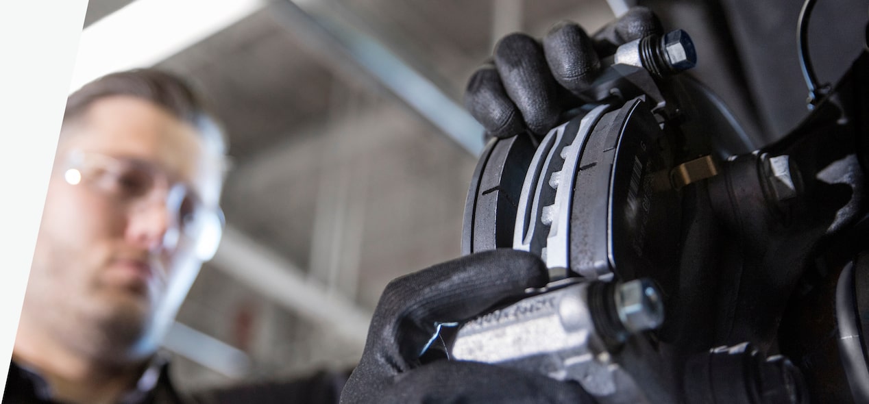A Below View of a Mechanic Wearing Protective Eyewear And Gloves Inspecting Brake Components.