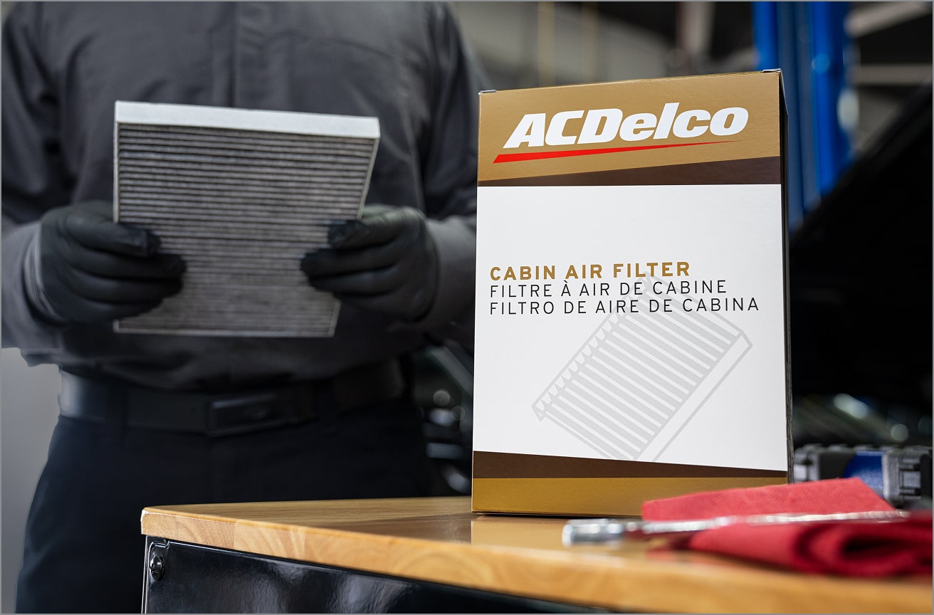 A Certified Technician Holding a Cabin Air Filter with the Box on the Table Next to Him.