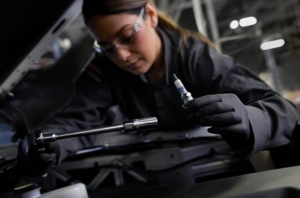 GM Technician Holding a Spark Plug and Working on a Vehicle
