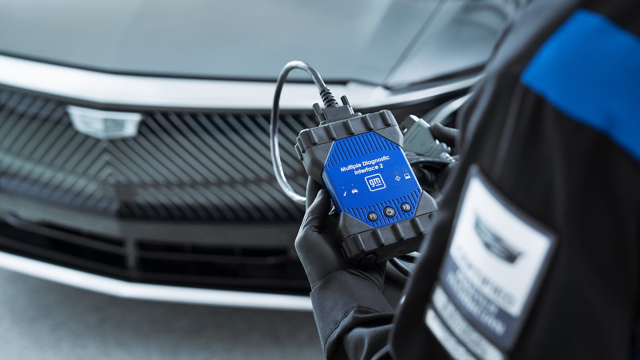 GM Technician Holding the Multiple Diagnostic Interface 2 Tool Standing In Front of a Cadillac Vehicle