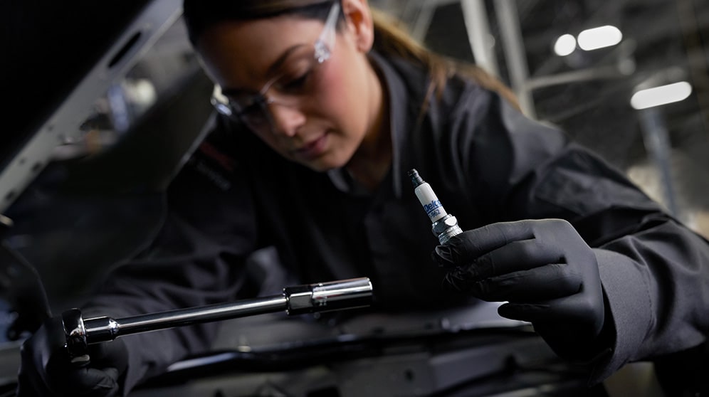 A Woman Mechanic Working on a Vehicle While Holding an ACDelco Spark Plug
