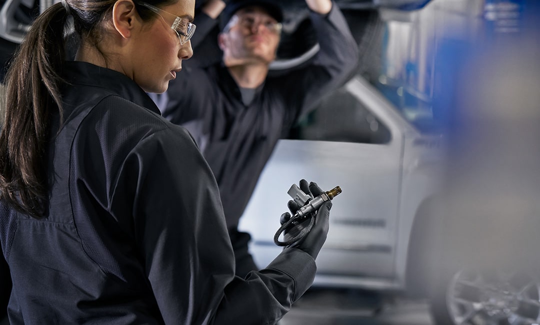 A Mechanic Wearing Protective Glasses Holding a Metal Vehicle Part and Observing It