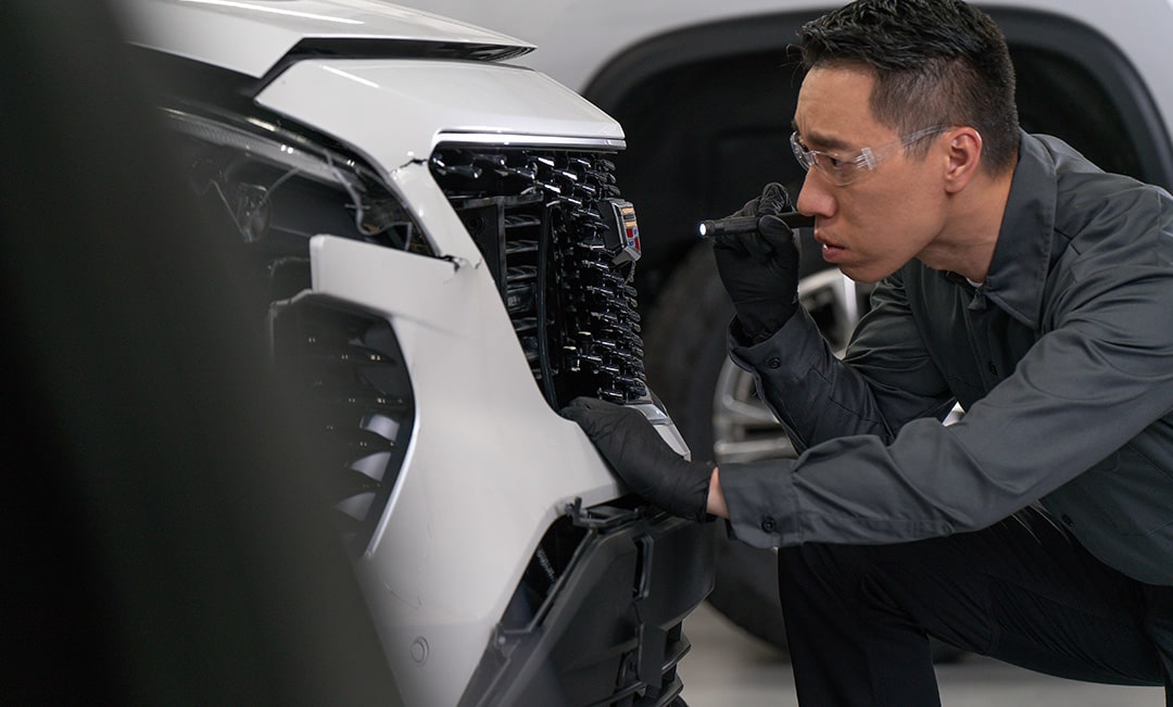 Side View of a Mechanic Inspecting the Front Grill of a White Vehicle