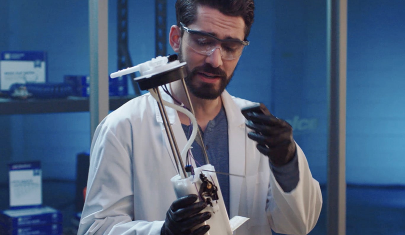 A Man Wearing a Lab Coat and Goggles Tests an Automotive Part